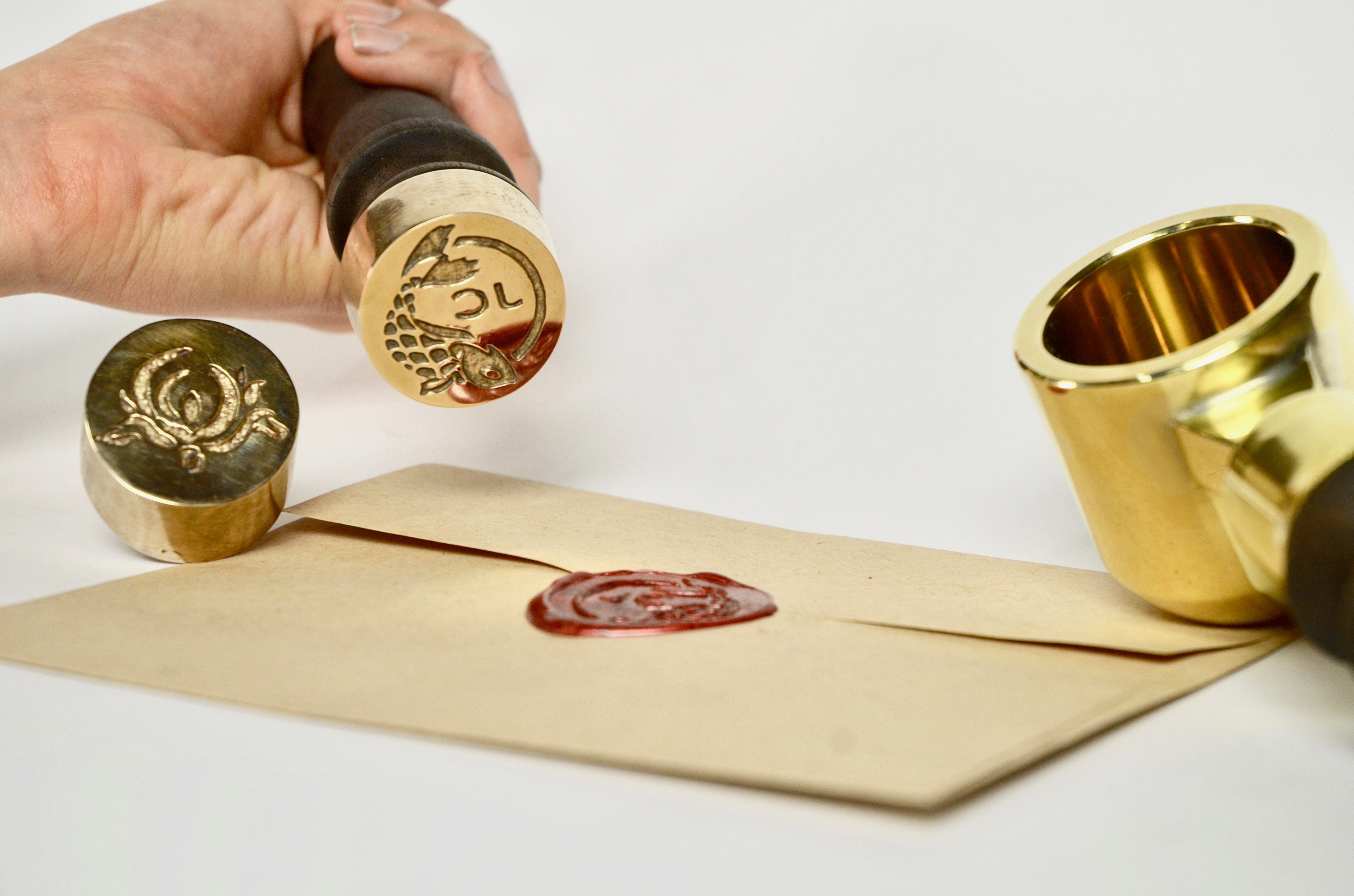 bronze stamps with a koi fish and flower design stamping a brown envelope with a wax red seal