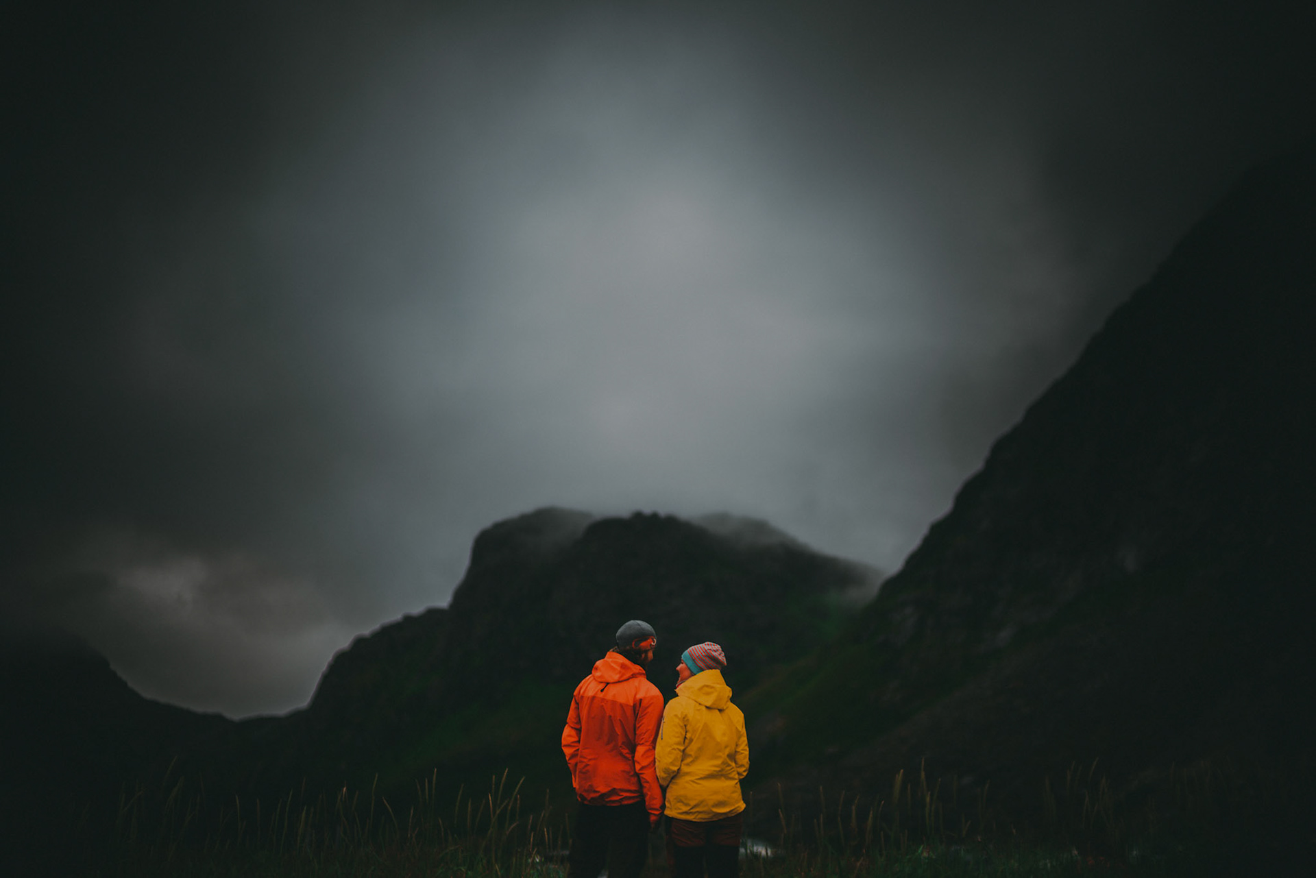 A couple wearing outdoor hiking apparel in front of foggy hilltops, Lofoten Islands, Norway, July 2016, Sony A7RII.