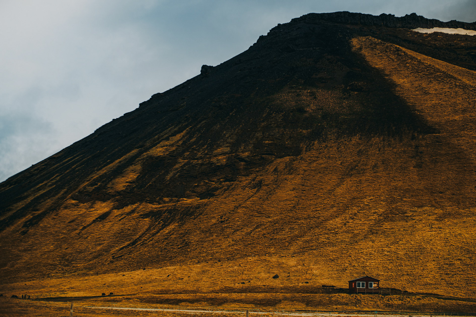 A landscape photo of a lone cabin on the foot of a triangular shaped slope, Iceland, May 2016, Sony A7RII.