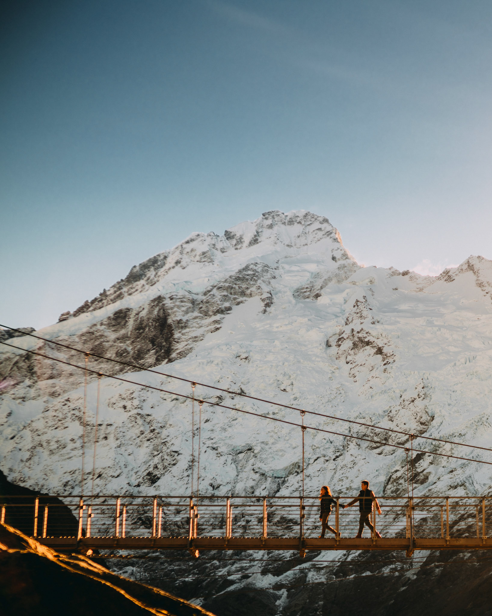A couple on a bridge with a snowy mountain peak in the background, Aoraki Mount Cook National Park, New Zealand, June 2017, Sony A7RII.