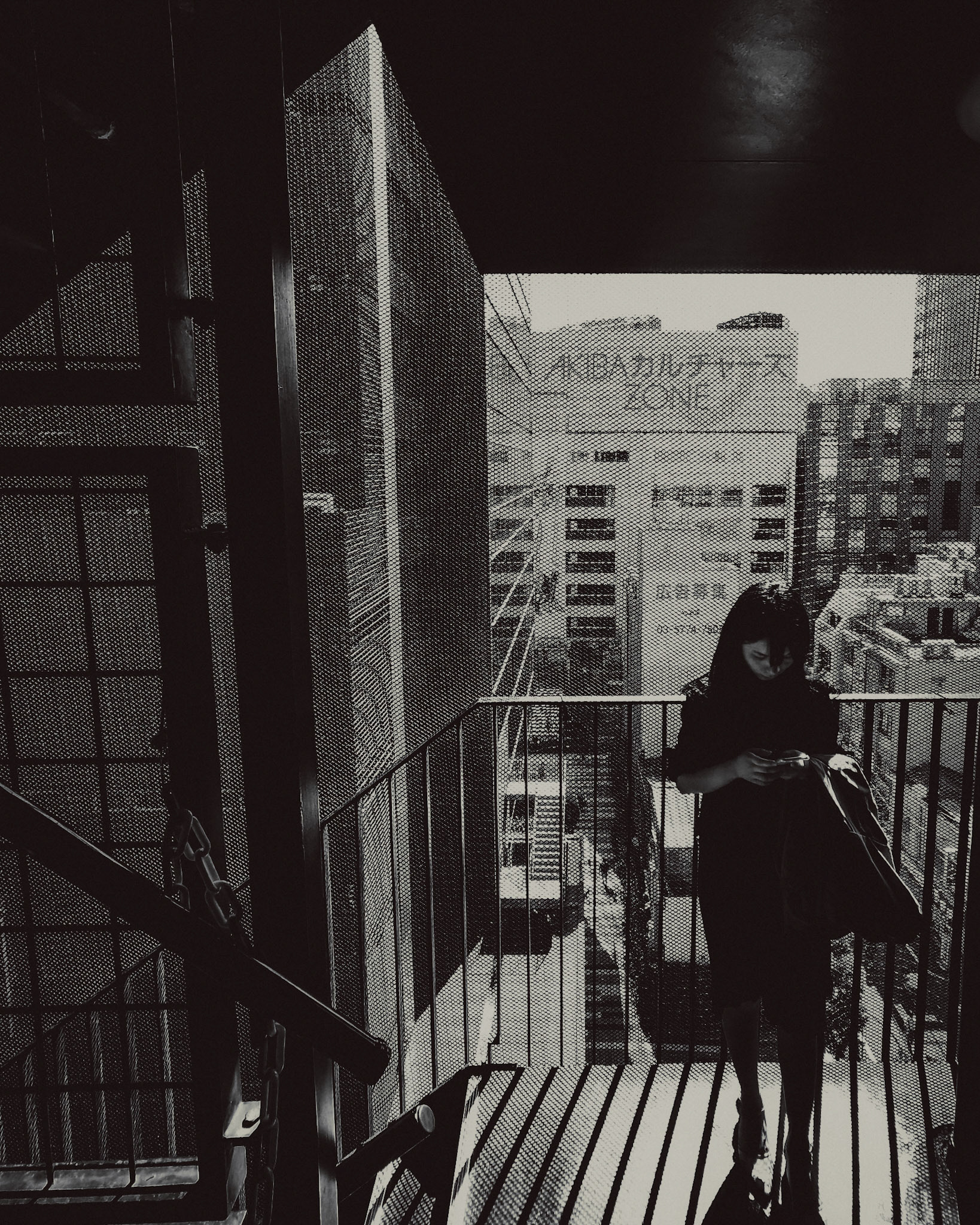A woman standing on a fire escape, in black and white, Akihabara, Tokyo, Japan, October 2019, Huawei P30 Pro.