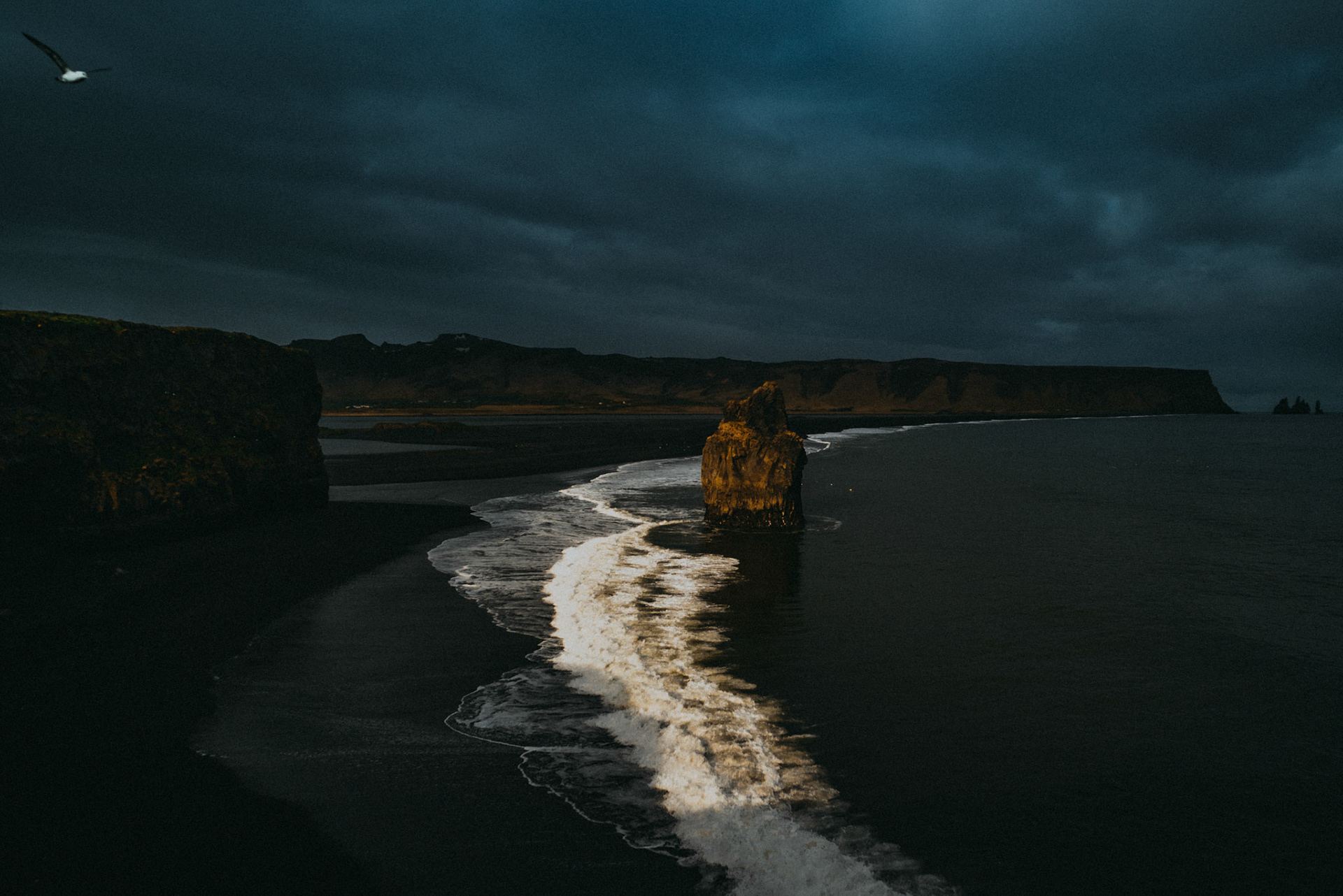A moody landscape photo of a black sand beach and rocky cliffs from Dyrhólaey Viewpoint, Iceland, May 2016, Sony A7SII.