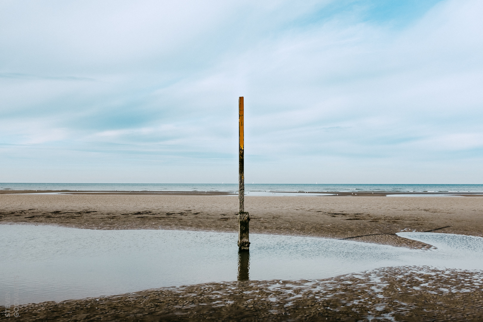 Op het strand van Koksijde (vanaf de grens met Nieuwpoort tot in Sint-Idesbald) staat een rij meetpalen. Bij laag tij komen ze zo goed als volledig droog te staan. Is het vloed, dan kan je doorgaans nog net het topje boven de golven zien uitsteken. Op één of andere manier hebben ze een bepaalde aantrekkingskracht op mij en ik heb ze al vanuit -tig hoeken gefotografeerd. Heb je in 2012 het kunstproject Getij-Dingen02 bezocht, dan heb je misschien nog ergens diep verscholen in de schuif een programmaboekje liggen... met foto's van de palen door uw dienaar.