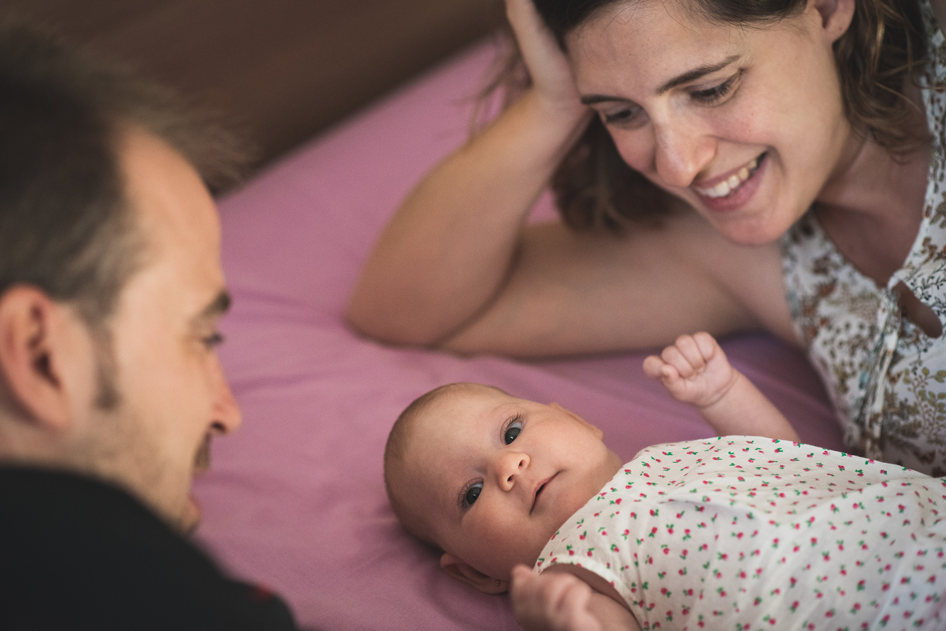 En la fotografía se ve una familia con su bebé. El bebé sonríe y los papás están mirando y felices.