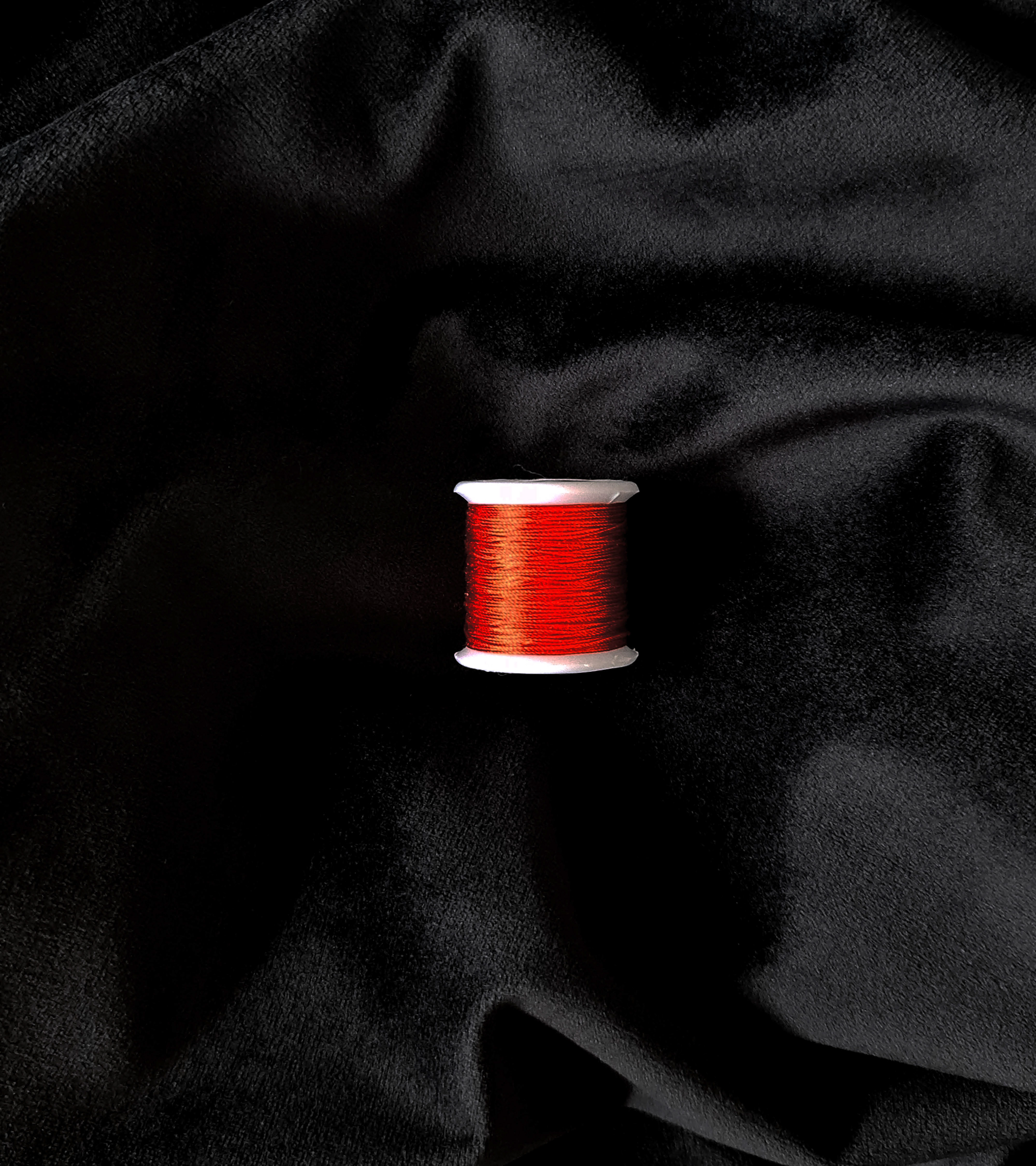 Image of Chinese red silk spool laying on top of black velvet.