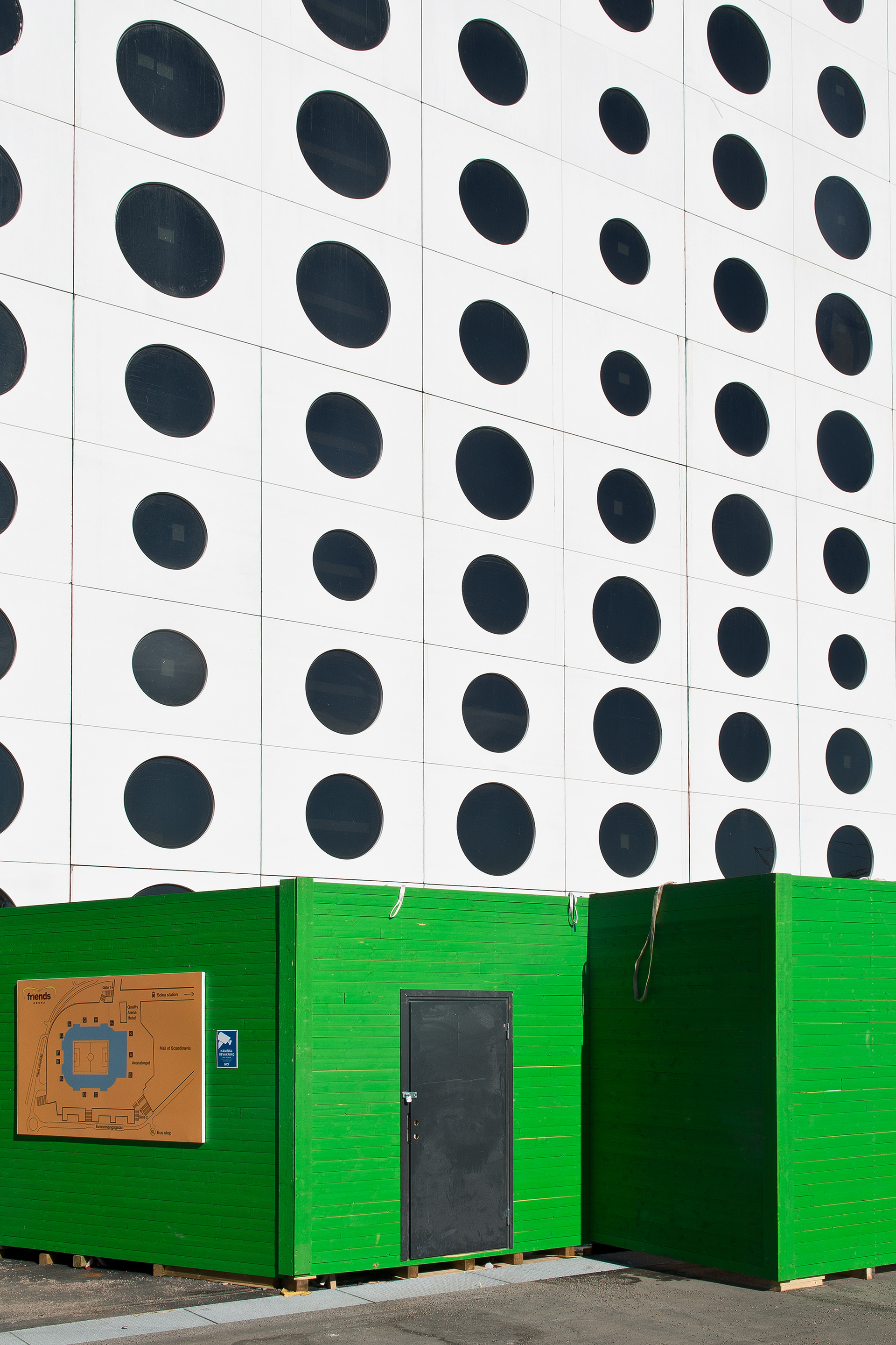 Short green wooden facade in front of Quality Friends Hotel. A white wall with round windows