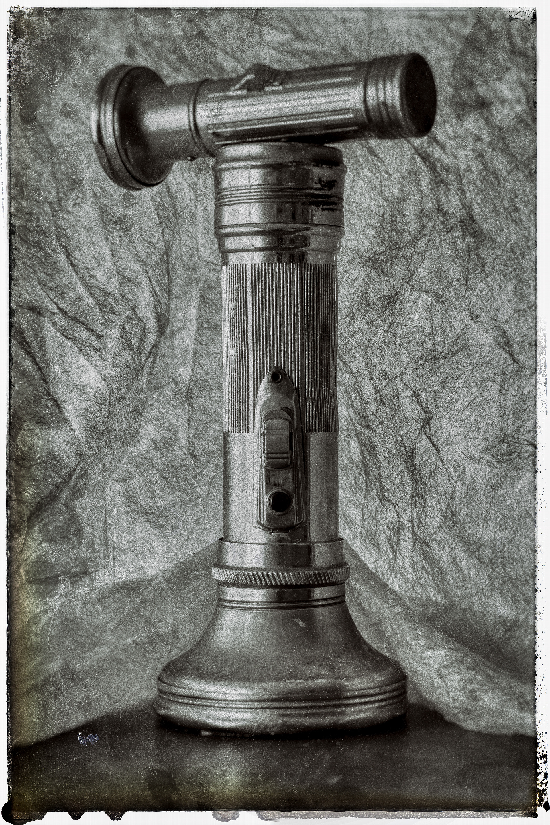 2 aluminuim old vintage flashlights in different sizes against a light cloth. Photograpphed in black and white