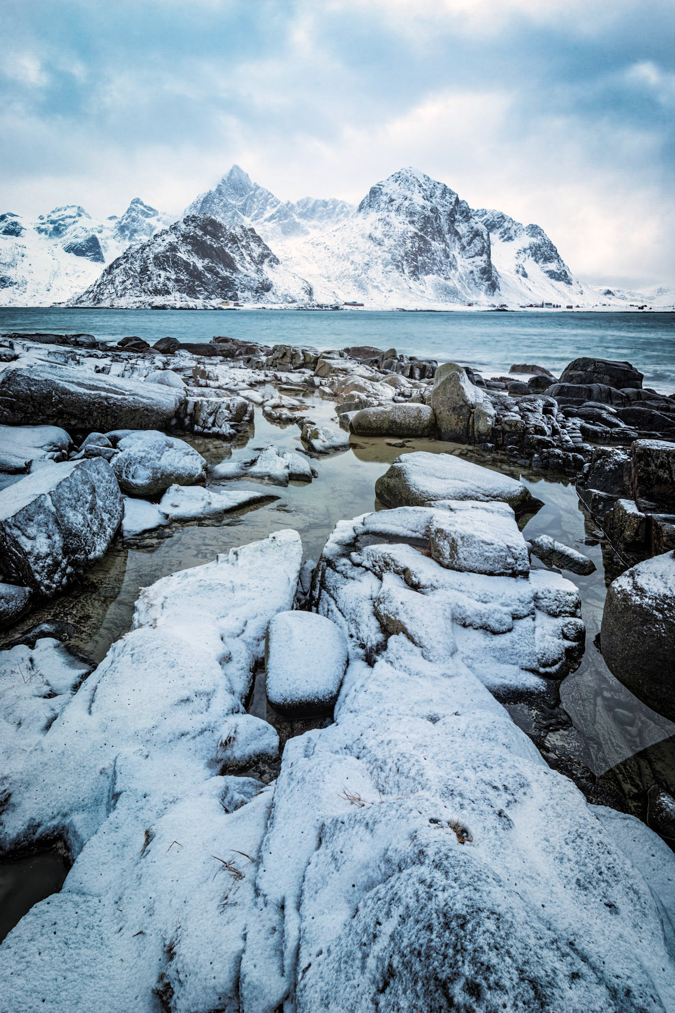 The rocky shoreline along Vareidsundet, leading into Flakstadpollen, with Stortinden and Flakstadtinden in the distance.Vareid, Nordland, NorwayMarch 19, 2018Pentax K-1, HD PENTAX-D FA 15-30mm F2.8ED SDM WRISO 100 22 mm  1.3 sec at ƒ / 20