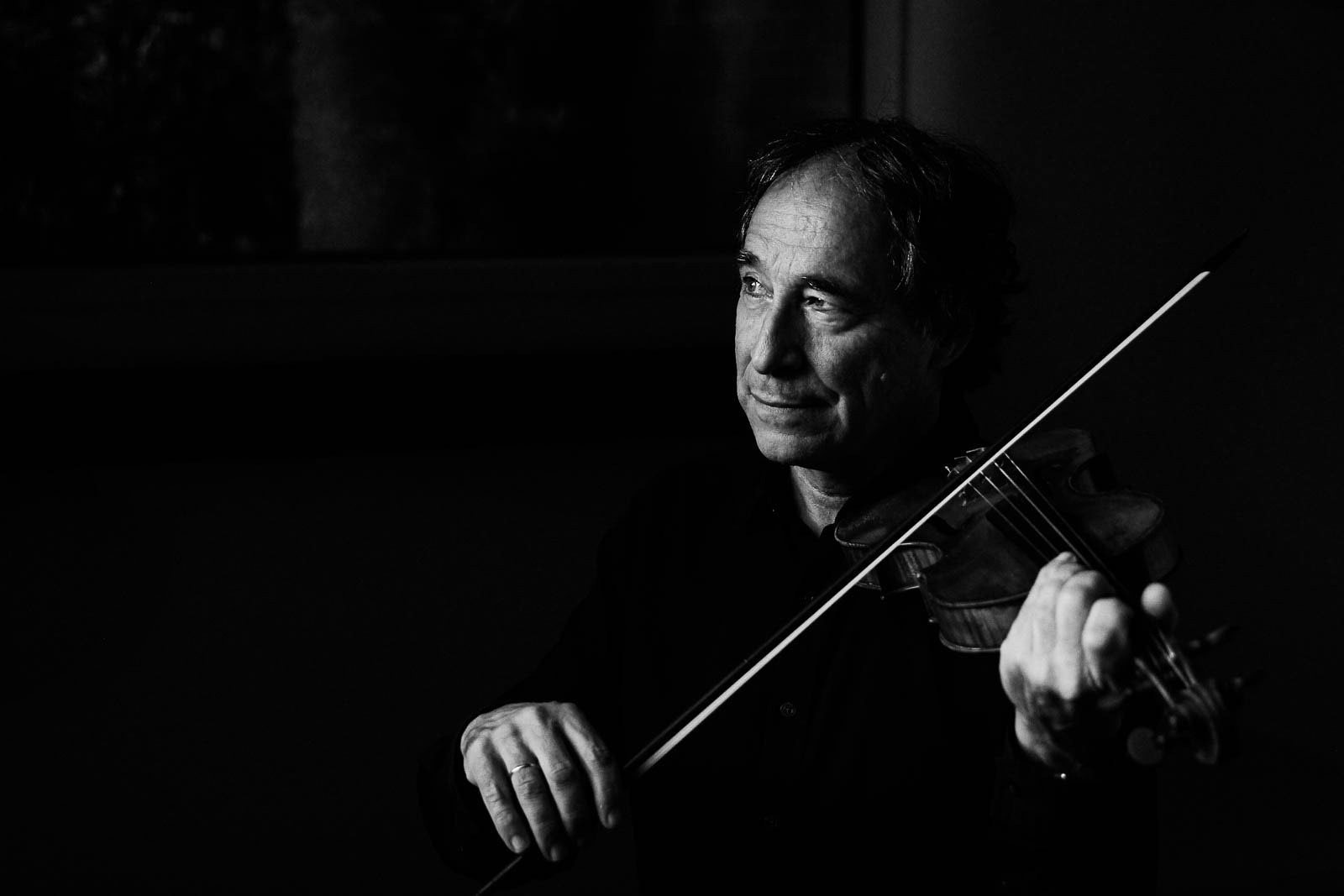 Violinist plays softly in dramatic lighting, looking off into the distance