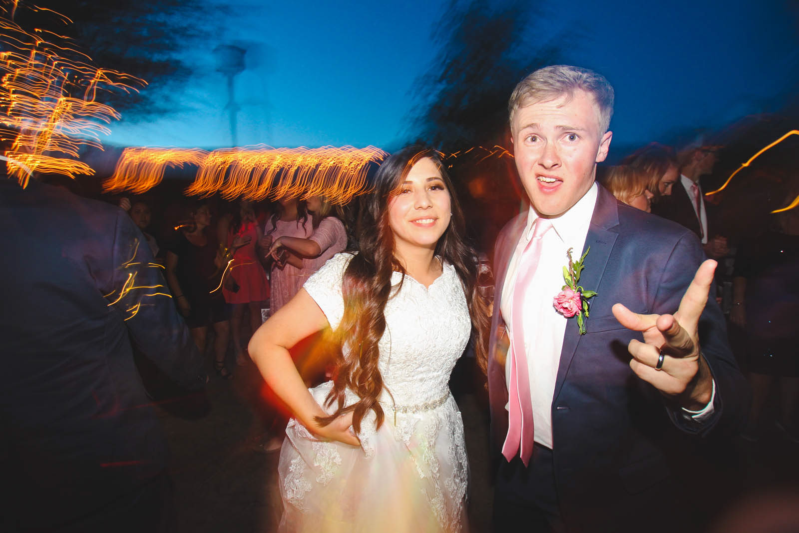 Wedding reception dance party at dusk, groom gestures toward camera