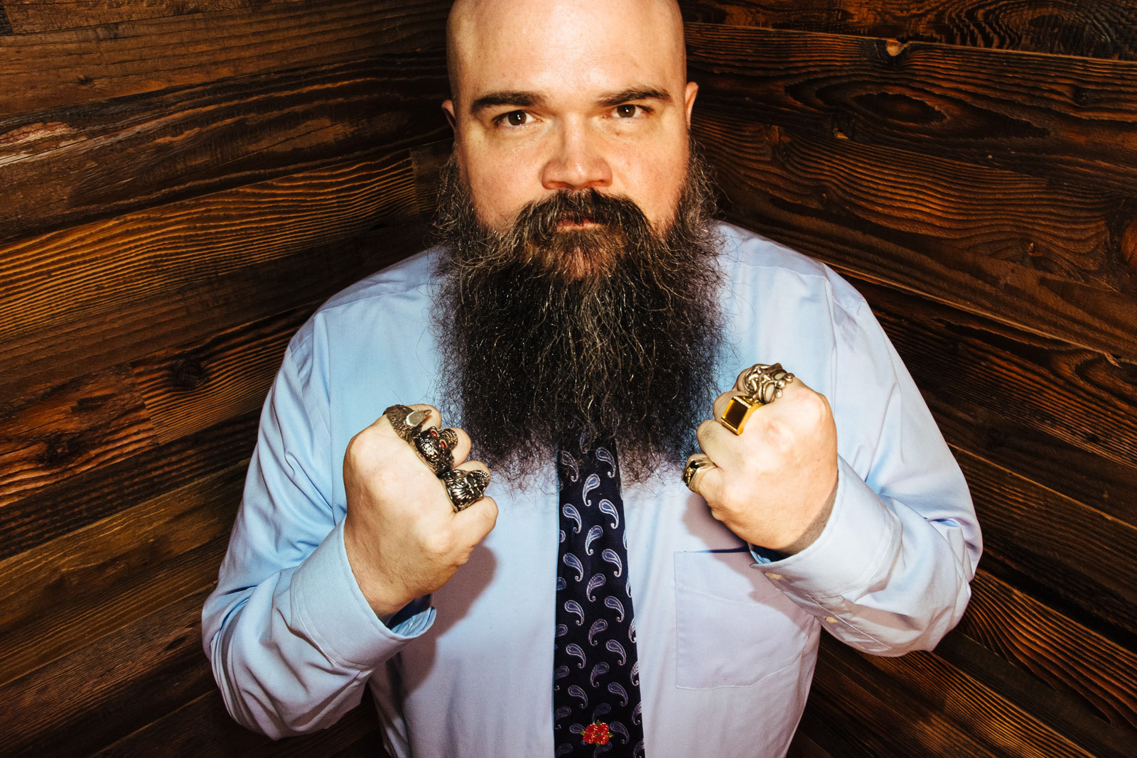 Bearded man stares out fiercely with clenched fists covered in large rings