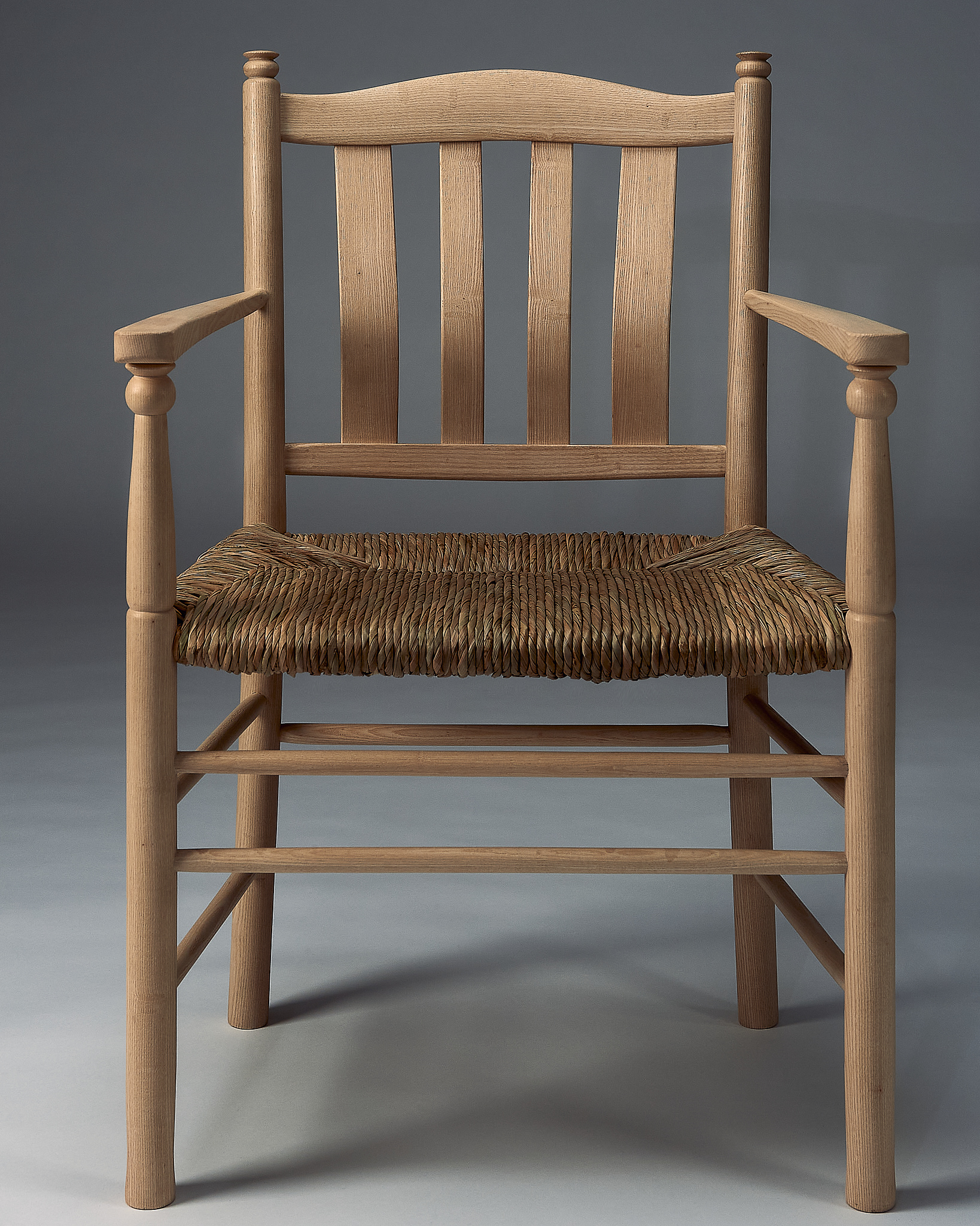 straight on photo of a wooden chair made from ash, a light-coloured wood, with a natural rush seat