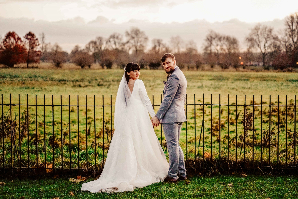newly married couple in candid photo by david lefebvre stood by oxfordshire field near town hall after covid wedding in december during golden hour