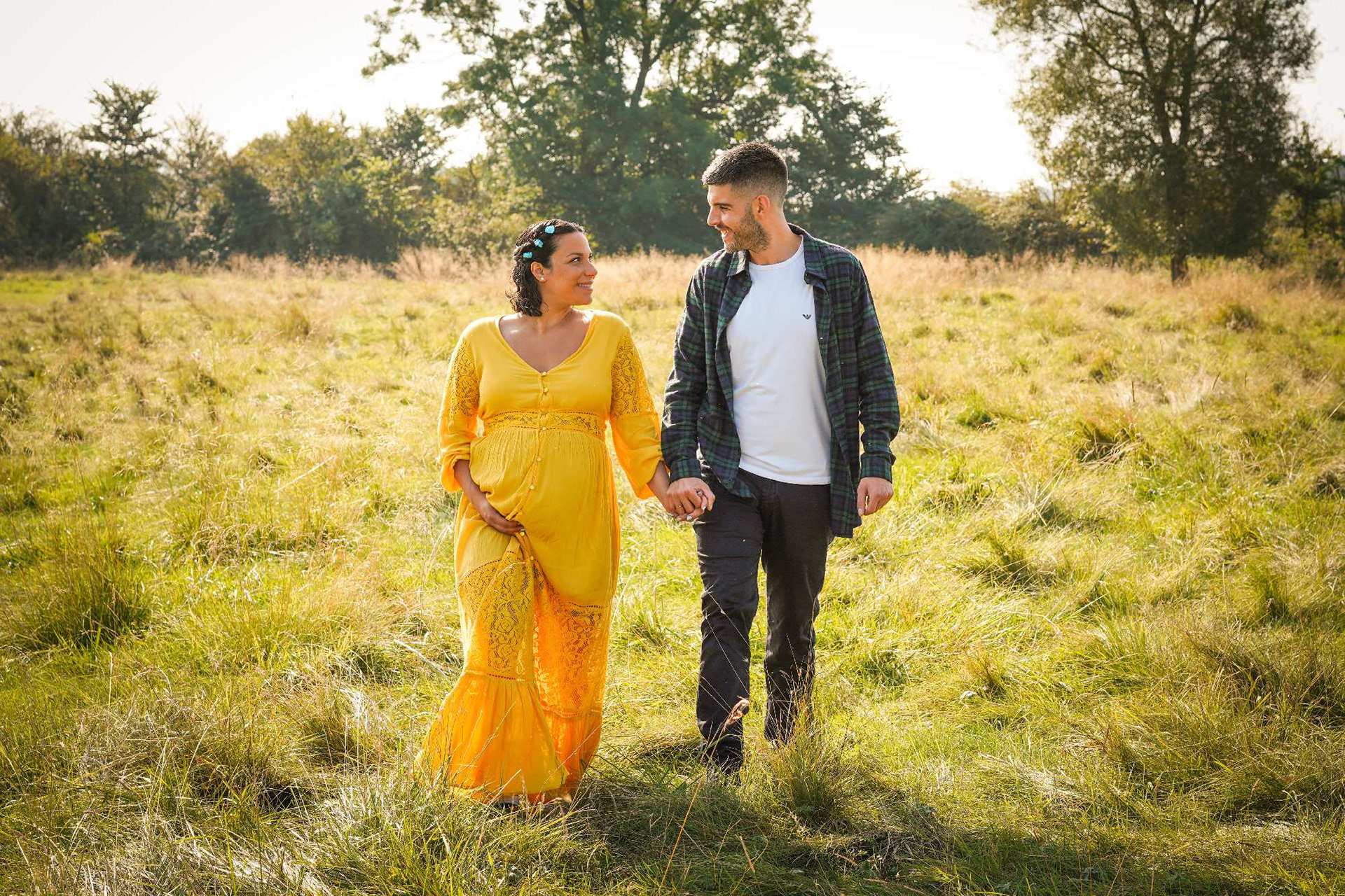 luxury gift idea for soon to be mum and partner walking through field in buckinghamshire smiling at each other wearing yellow dress and checkered shirt with photographer david lefebvre