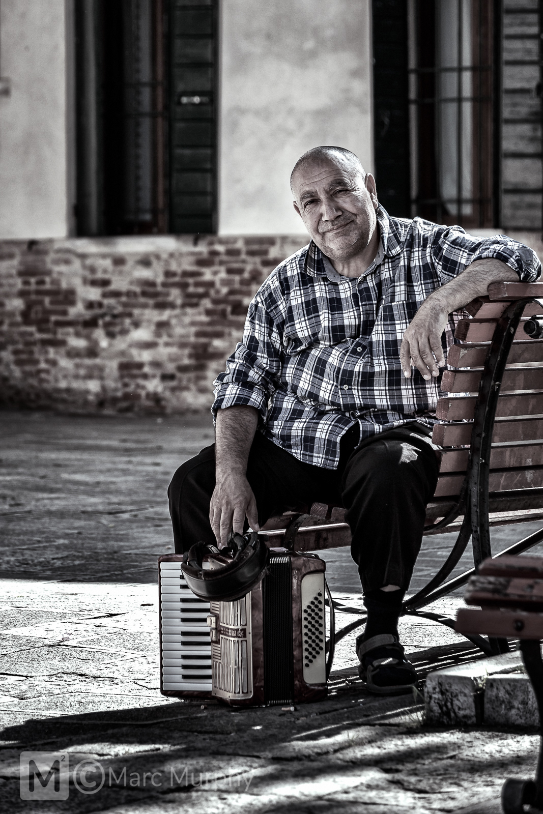 De-Saturated Italian Male Musician with His Accordion, Wearing Checkered Shirt and Sitting on a Bench in Venice Italy