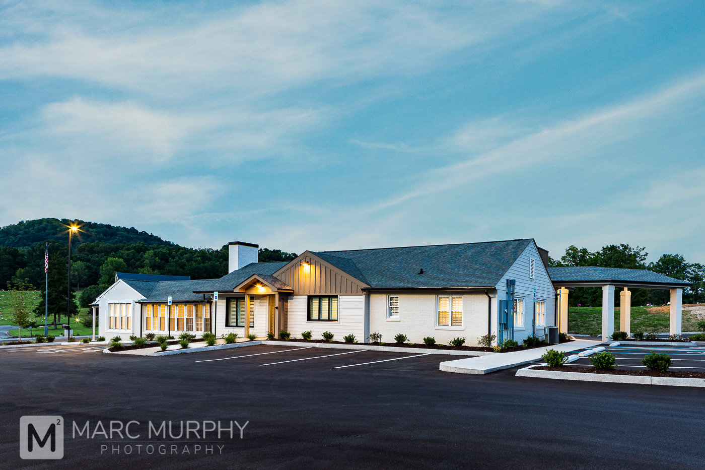 Exterior Single Story Monte Vista Memorial Park Brick and Glass Office Building and Mausoleum at Dusk with Interior Lights On, Parking Lot, White Clouds and Blue Sky