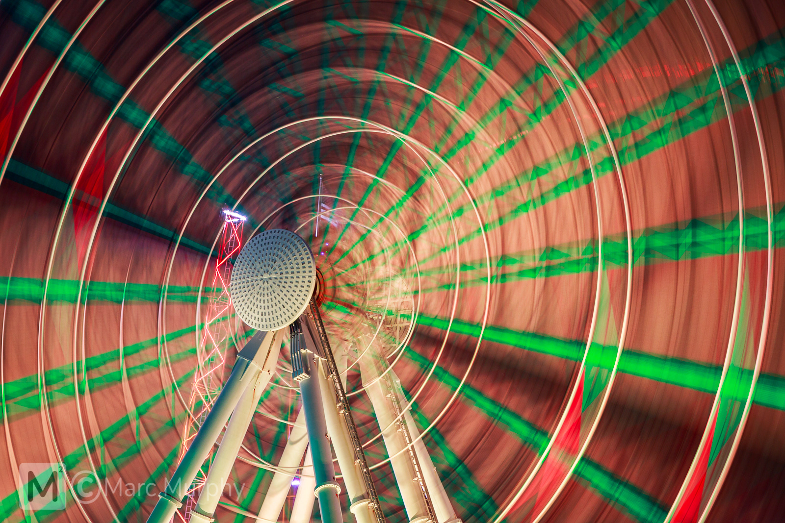 Red, Orange, Yellow and Green Ferris Wheel In Motion with White Steel Supporting Structure