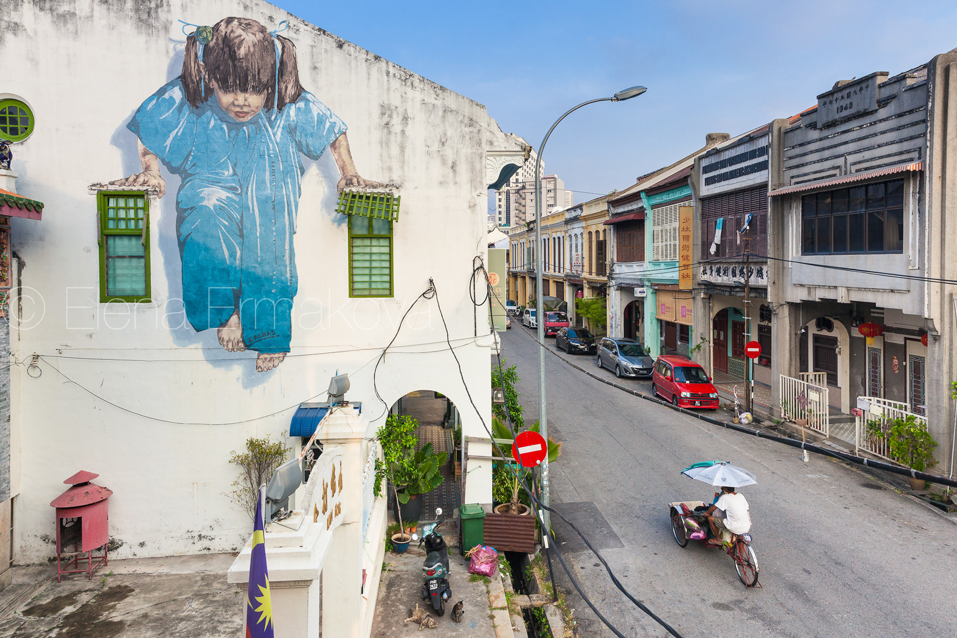 Cycle rickshaw is riding down the street in front of the famous street art painting on the wall. George Town, Penang, Malaysia. Travel photography by Elena Ermakova.