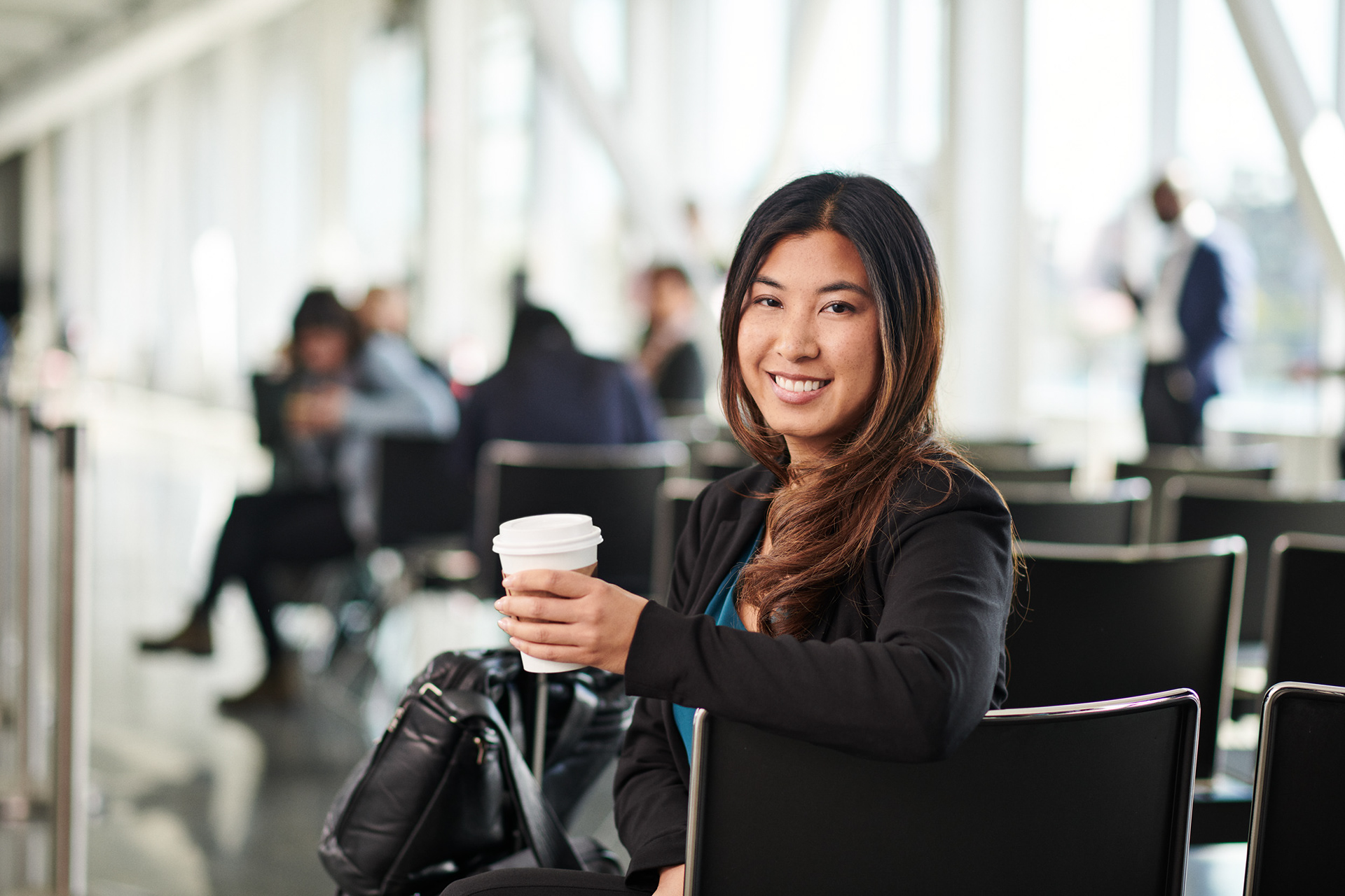portrait of a business woman holding a coffee, while sitting down waiting for her flight