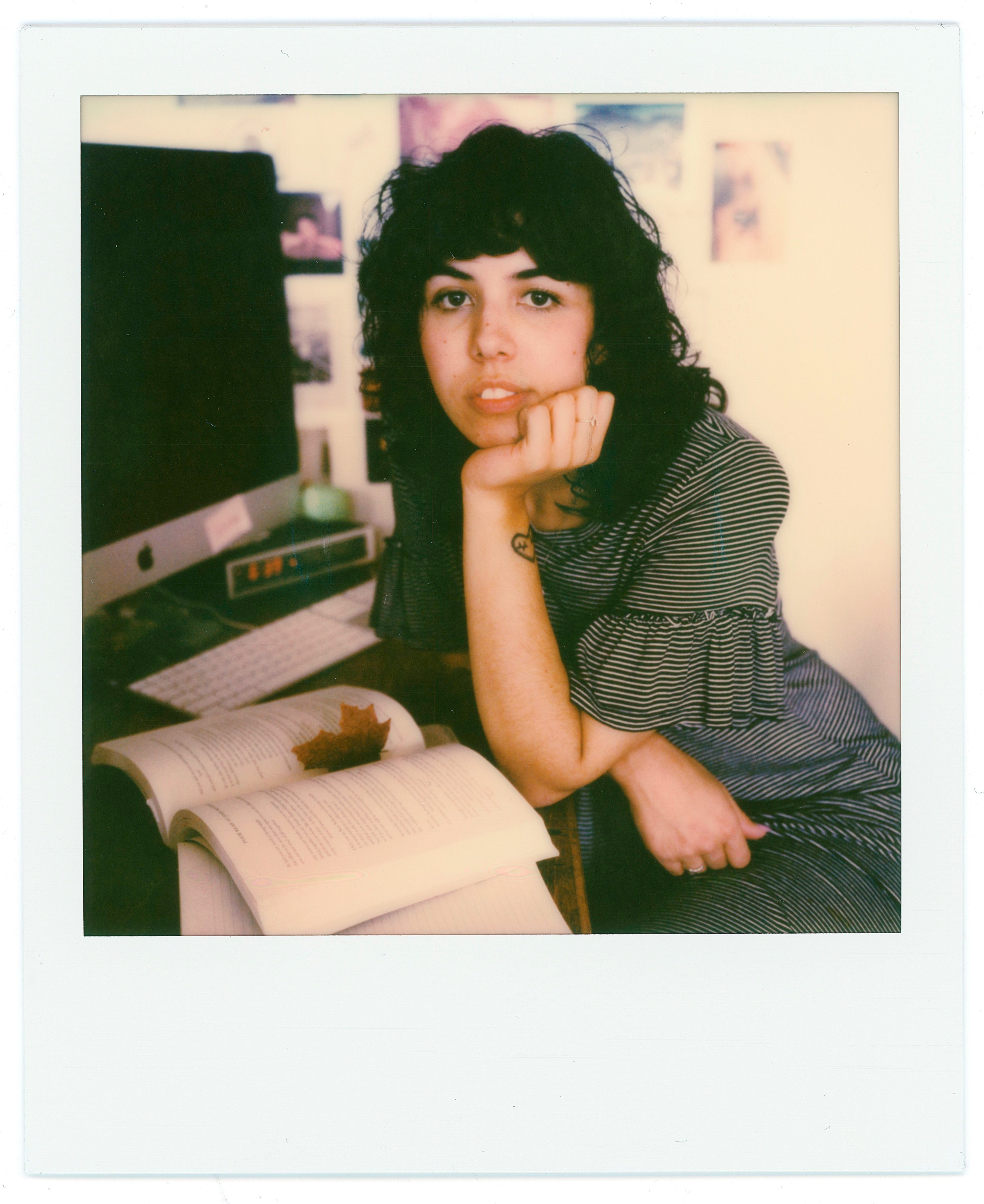 dark haired young woman at desk with computer and book containing a leaf