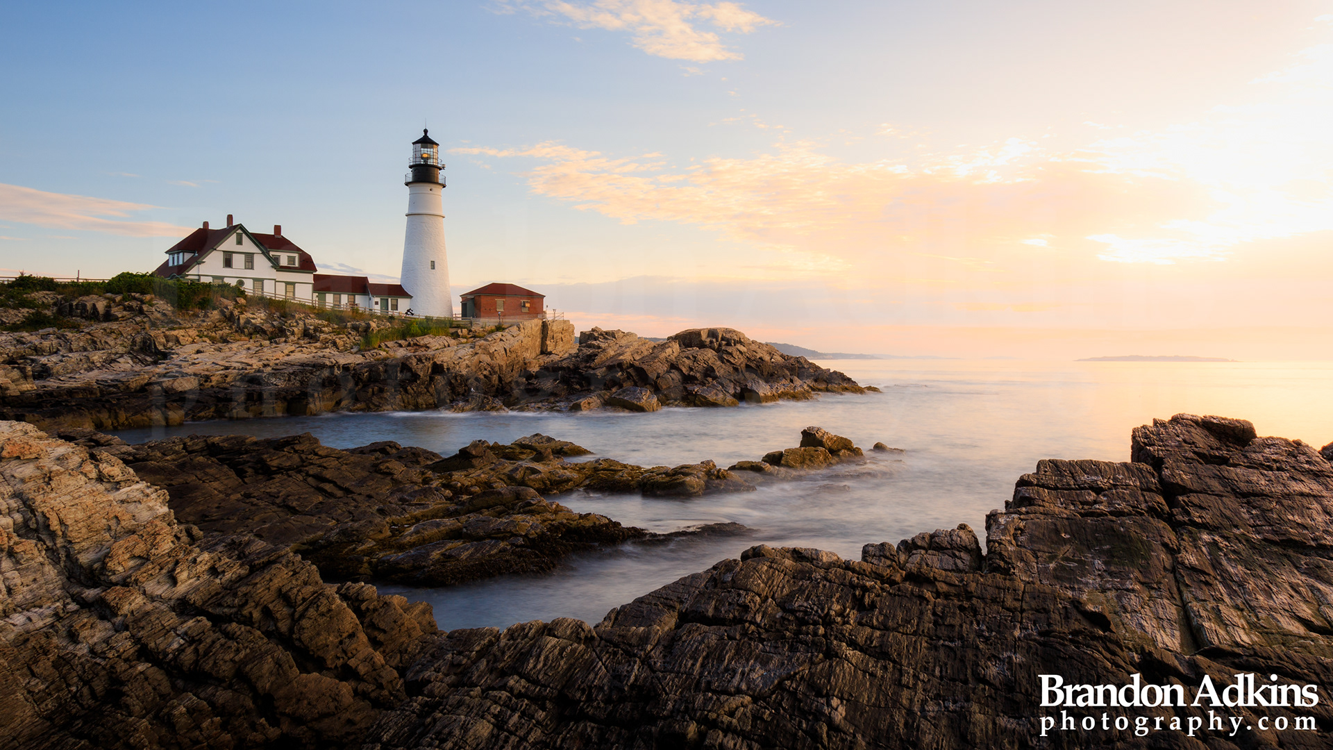 Fine art photograph of Portland Head Light lighthouse with rocky shoreline of Atlantic Ocean in foreground with beautiful sunrise in Fort Williams Park, Maine