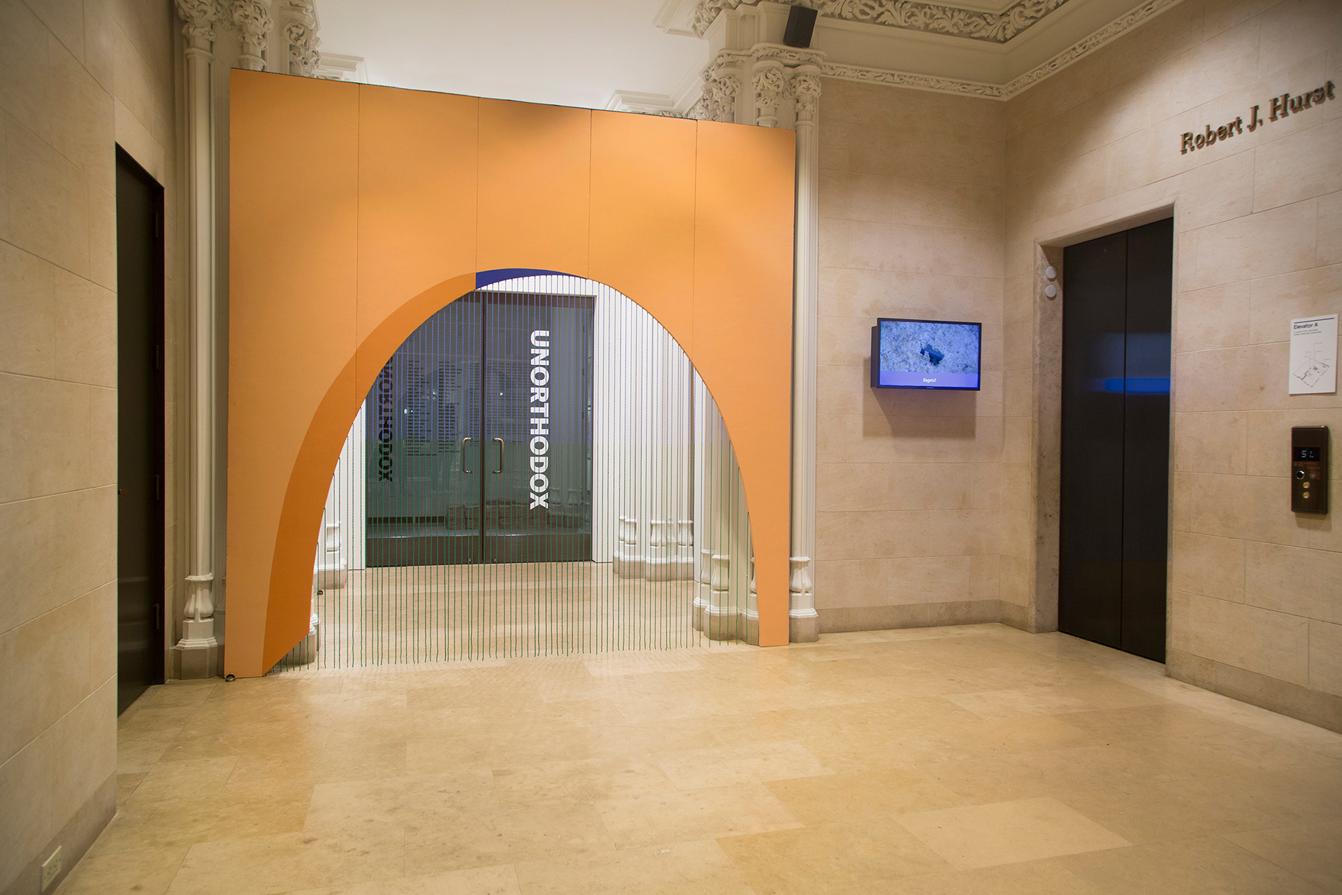An interration of "Paradise of Greenery" at the Jewish Museum in New York. The sculpture is an archway at the entry to the gallery space, constructed out of pink foam and painted orange. From the archway drips down a bead curtain that creates a horizon cut from blue beads at the top and green beads at the bottom.