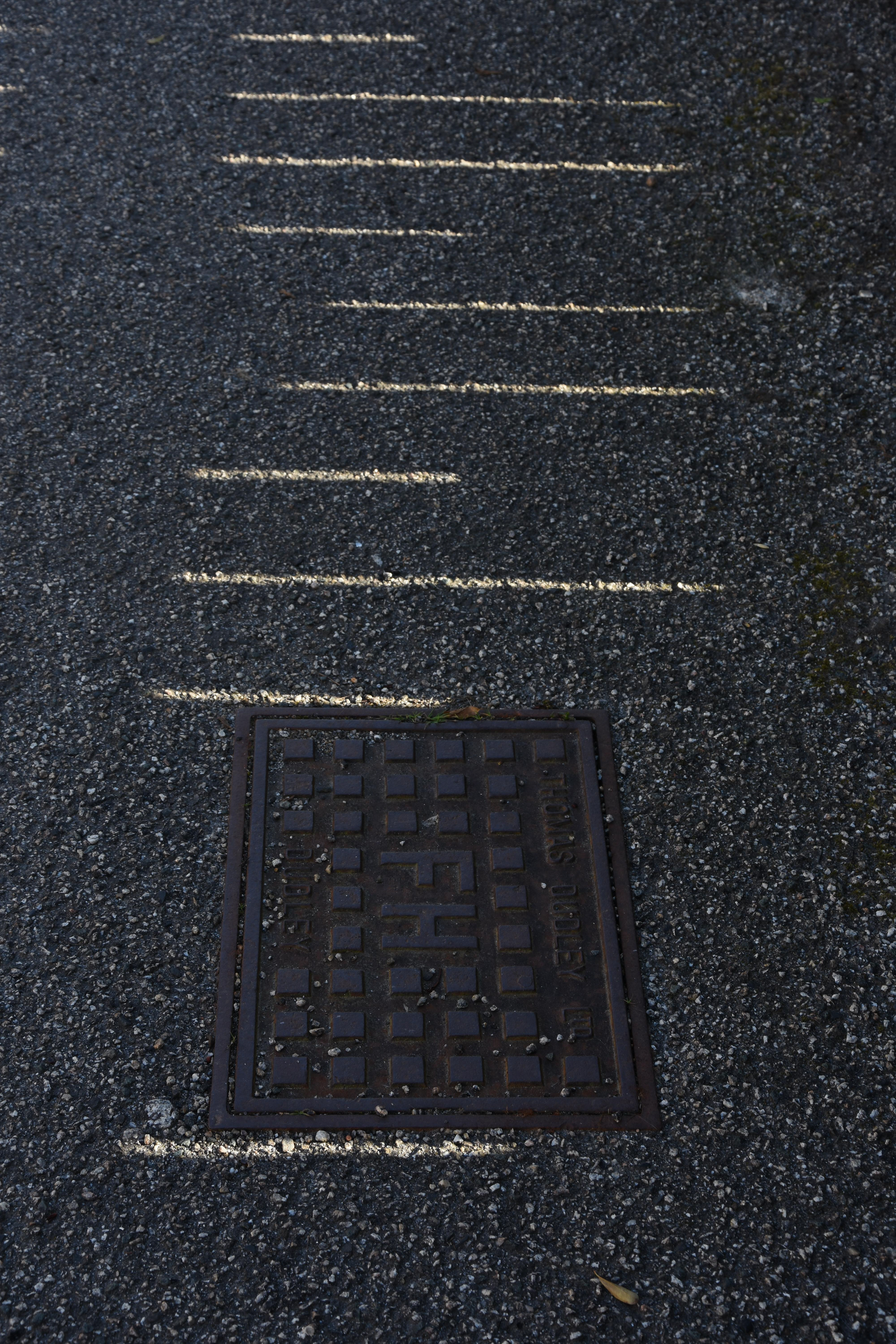 light and shadow casting on pavement with drain hold cover on a walk during covid 19 in cornwall